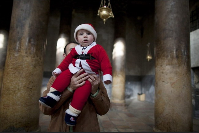 ชายคนหนึ่งกำลังชูหนูน้อยในชุดซานตาคลอสในโบสถ์